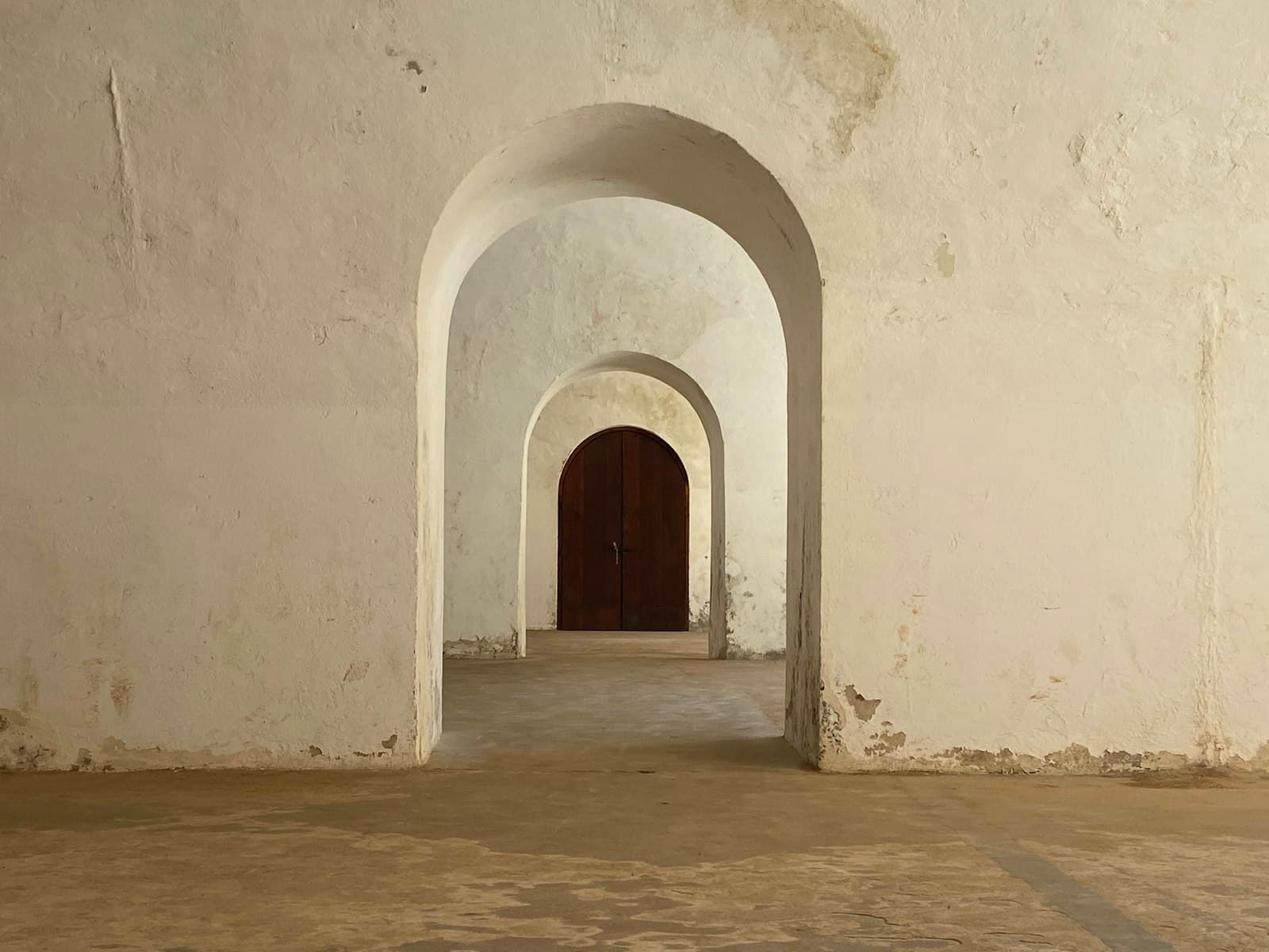 Una hilera de arcos encalados que conduce a una puerta de madera oscura