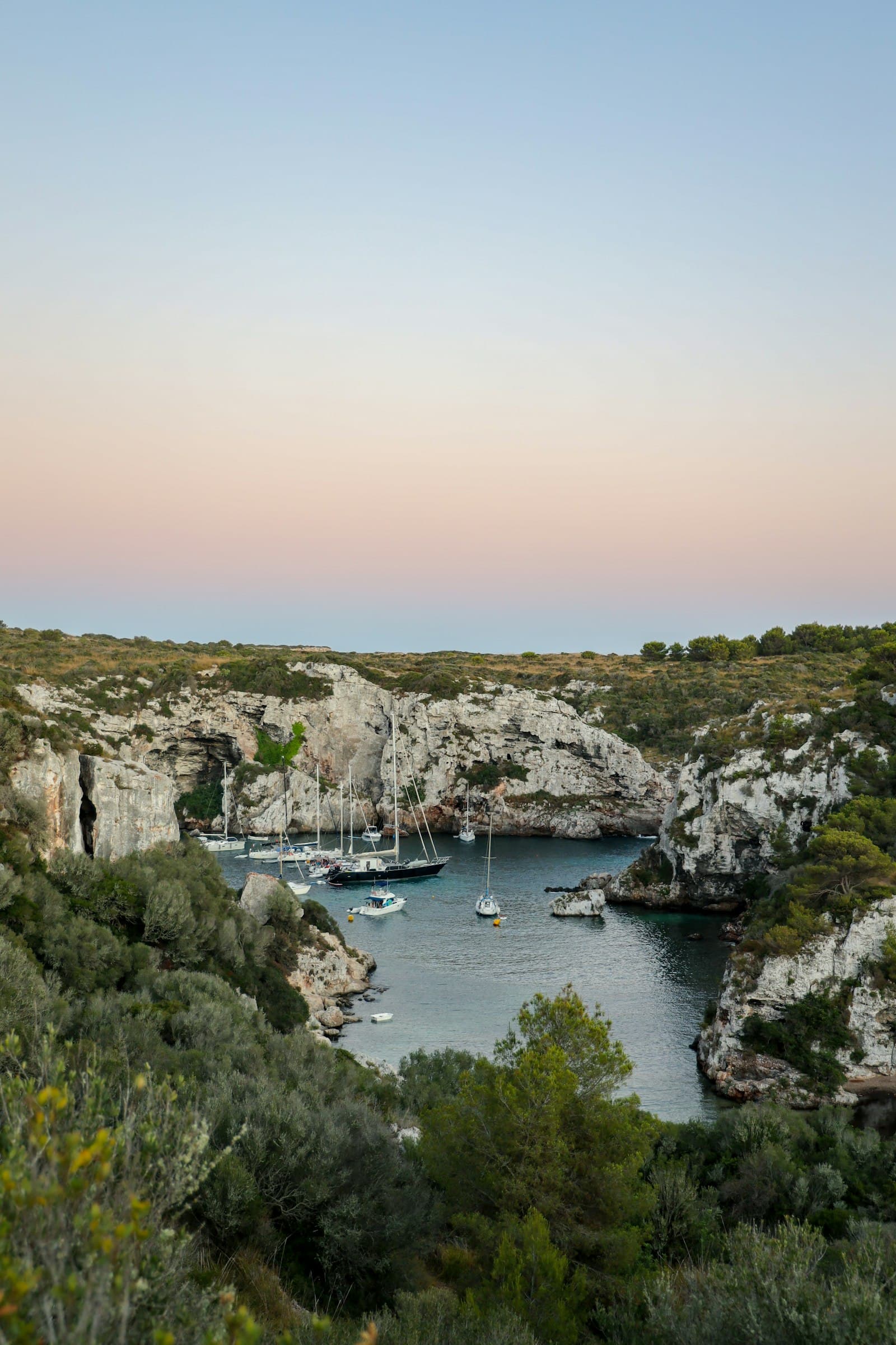 Una cala estrecha entre acantilados de caliza al atardecer, con barcas fondeadas