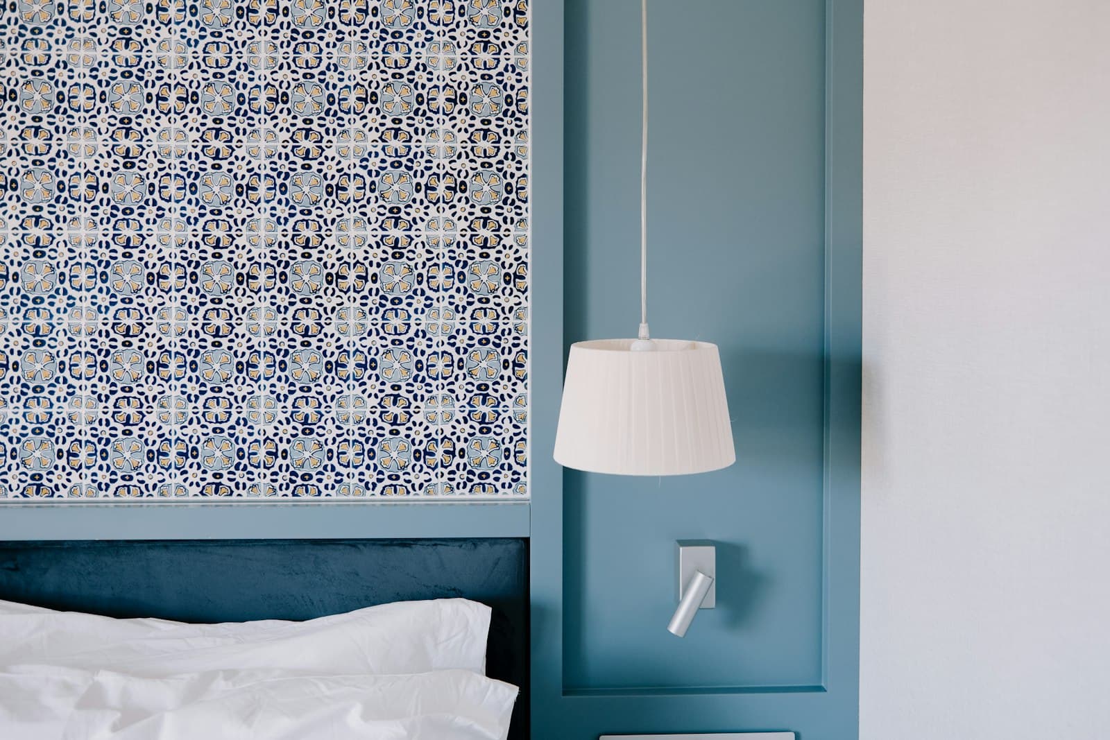 Un friso de madera pintado de azul, un cabecero de azulejos y una lámpara blanca plisada