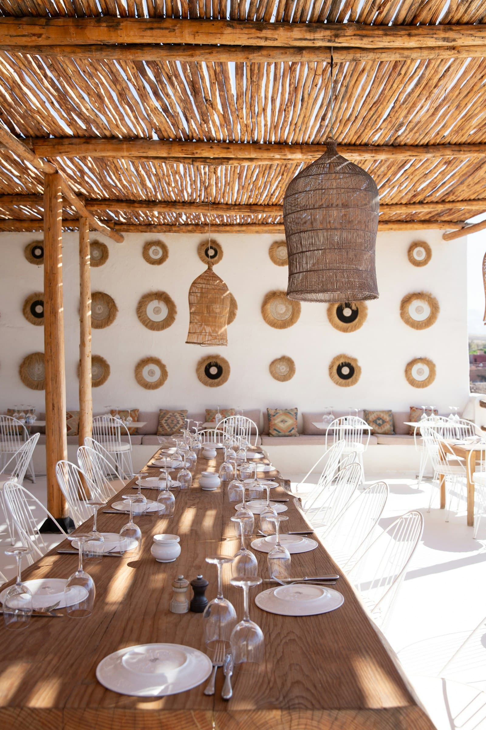 Una mesa larga de madera puesta con platos blancos y copas, bajo una luz tamizada