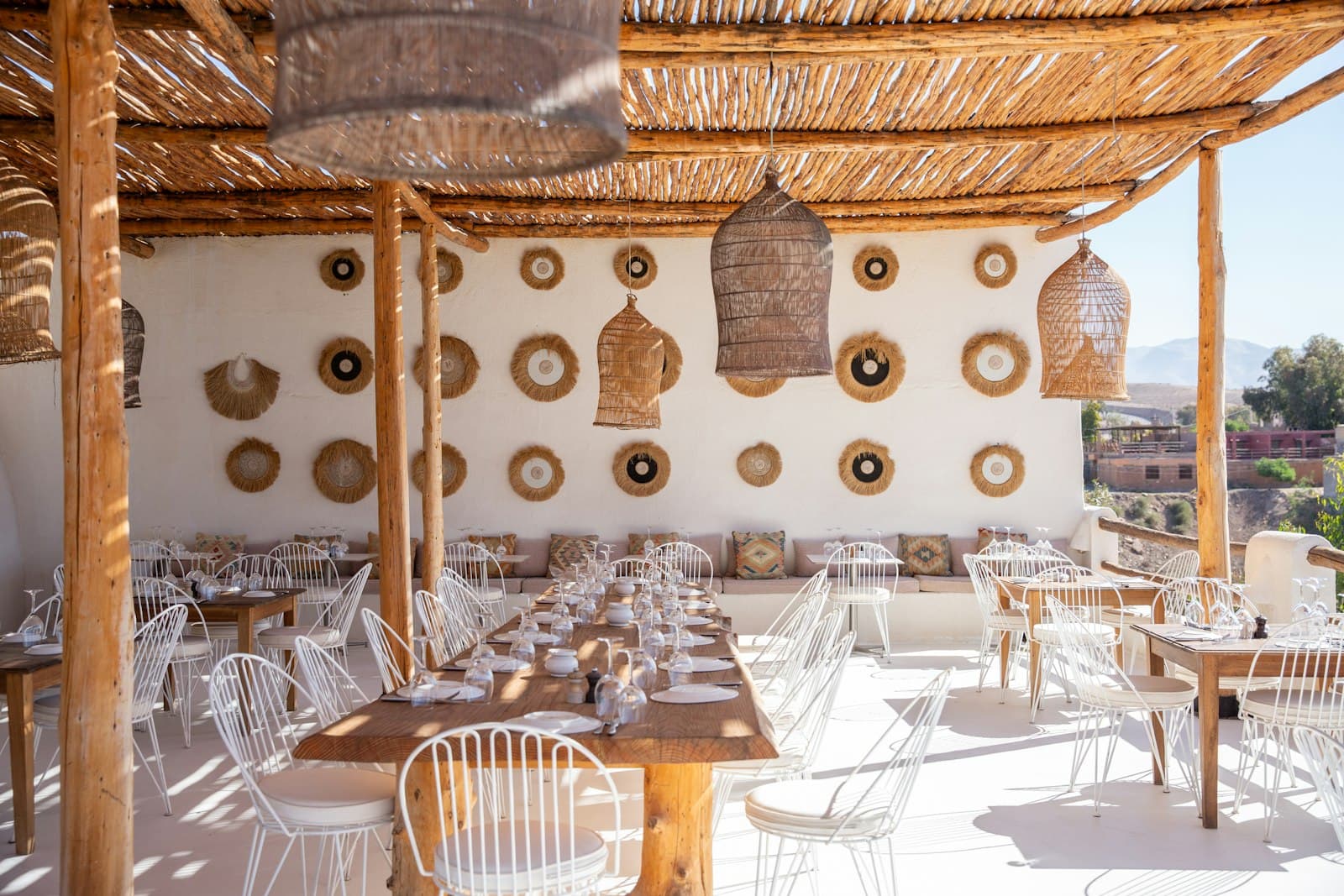 El restaurante de la azotea: sillas blancas de varilla y mesas de madera bajo una pérgola de caña con lámparas trenzadas