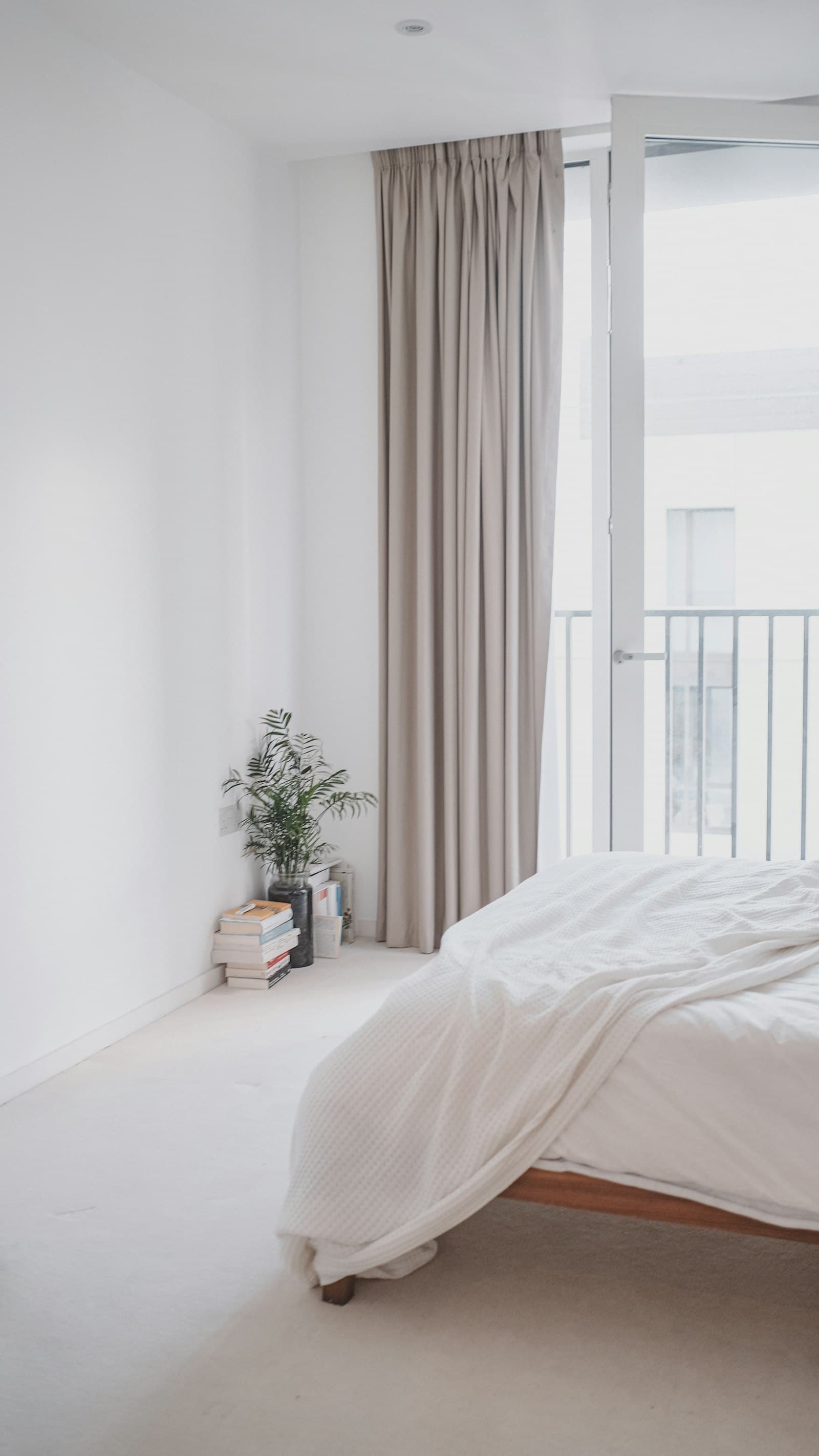 Dormitorio luminoso con una cama baja de lino junto a unas cortinas hasta el suelo y la puerta del balcón