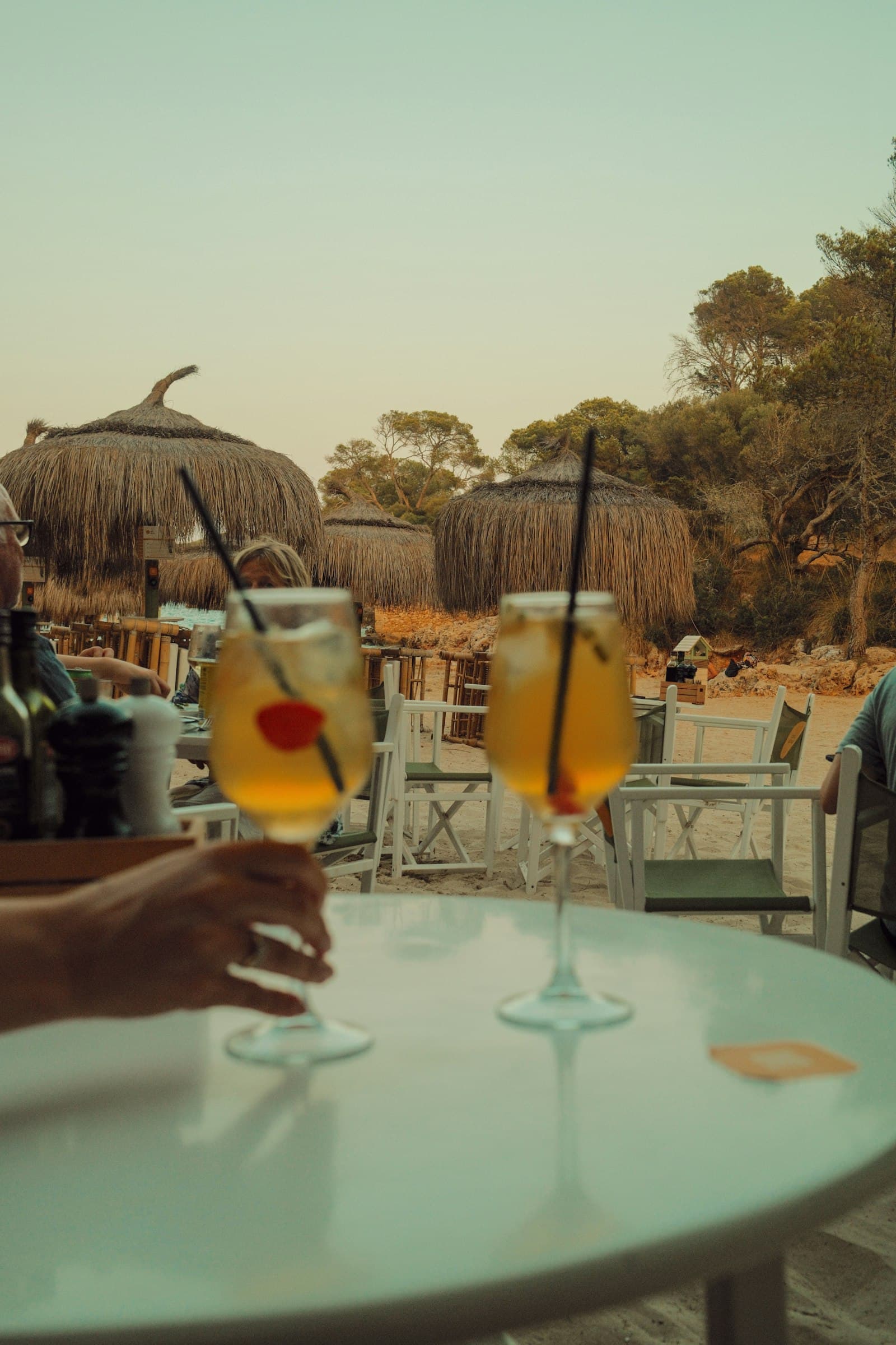Dos cócteles con hielo en una mesa redonda del bar de playa, con sombrillas de paja al fondo