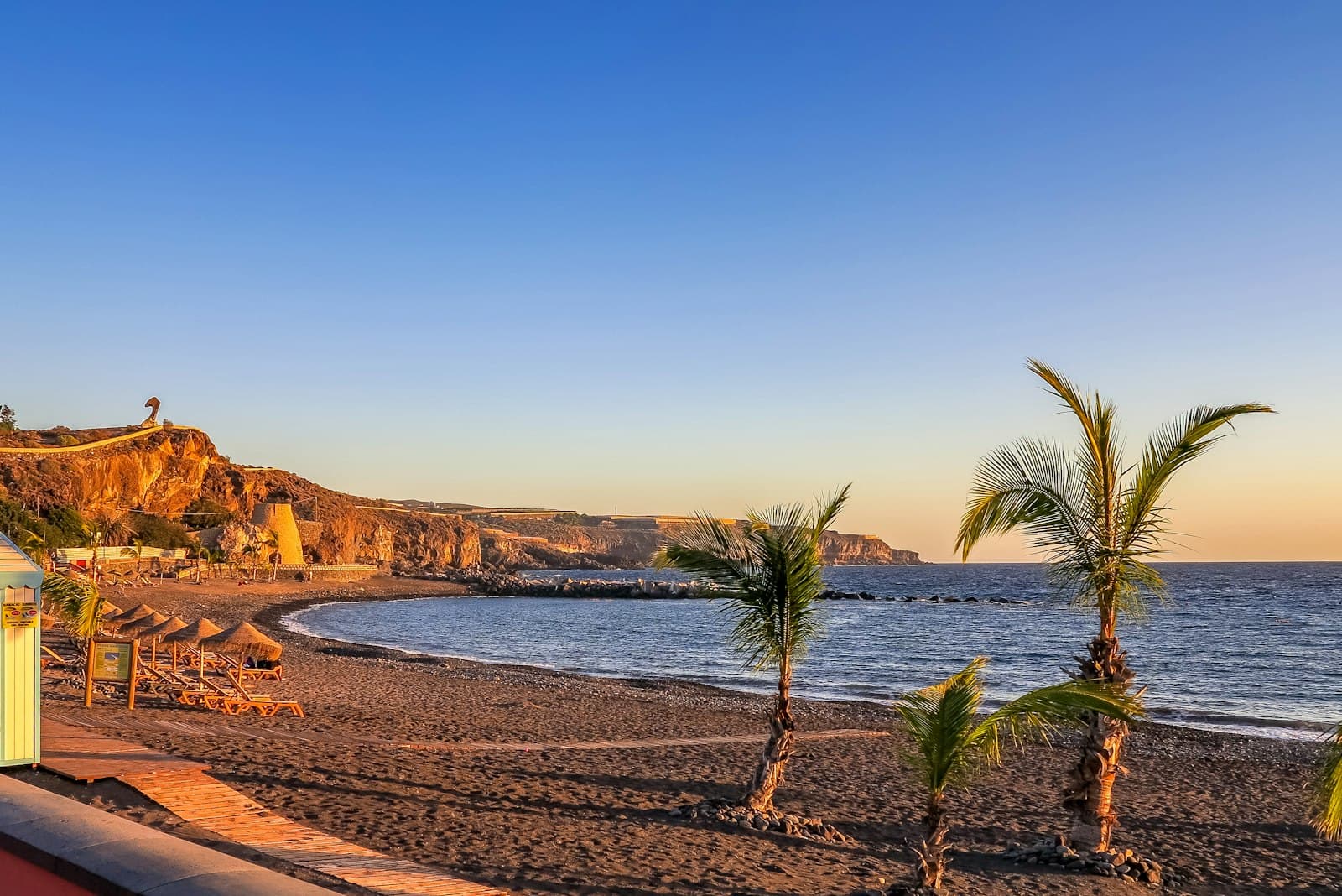 Playa Solmara a la hora dorada, con palmeras sobre la arena y los acantilados de Punta Faro al fondo