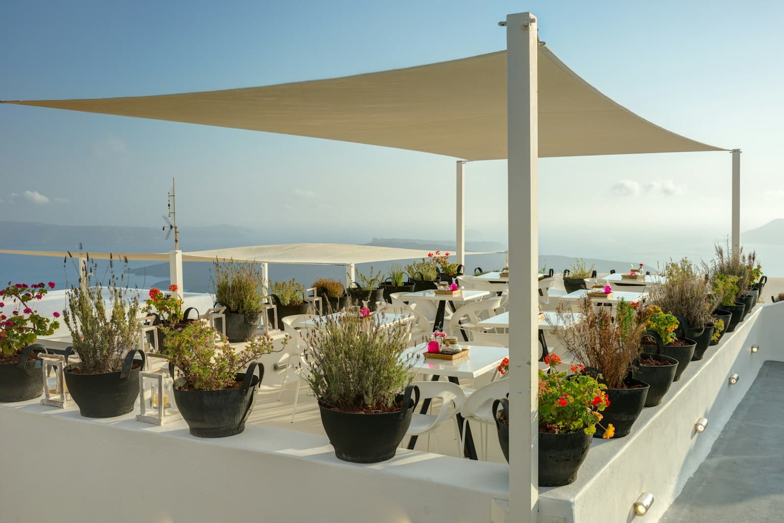 Restaurante en una terraza blanca bajo un toldo vela, bordeada de macetas de lavanda y con vistas al mar