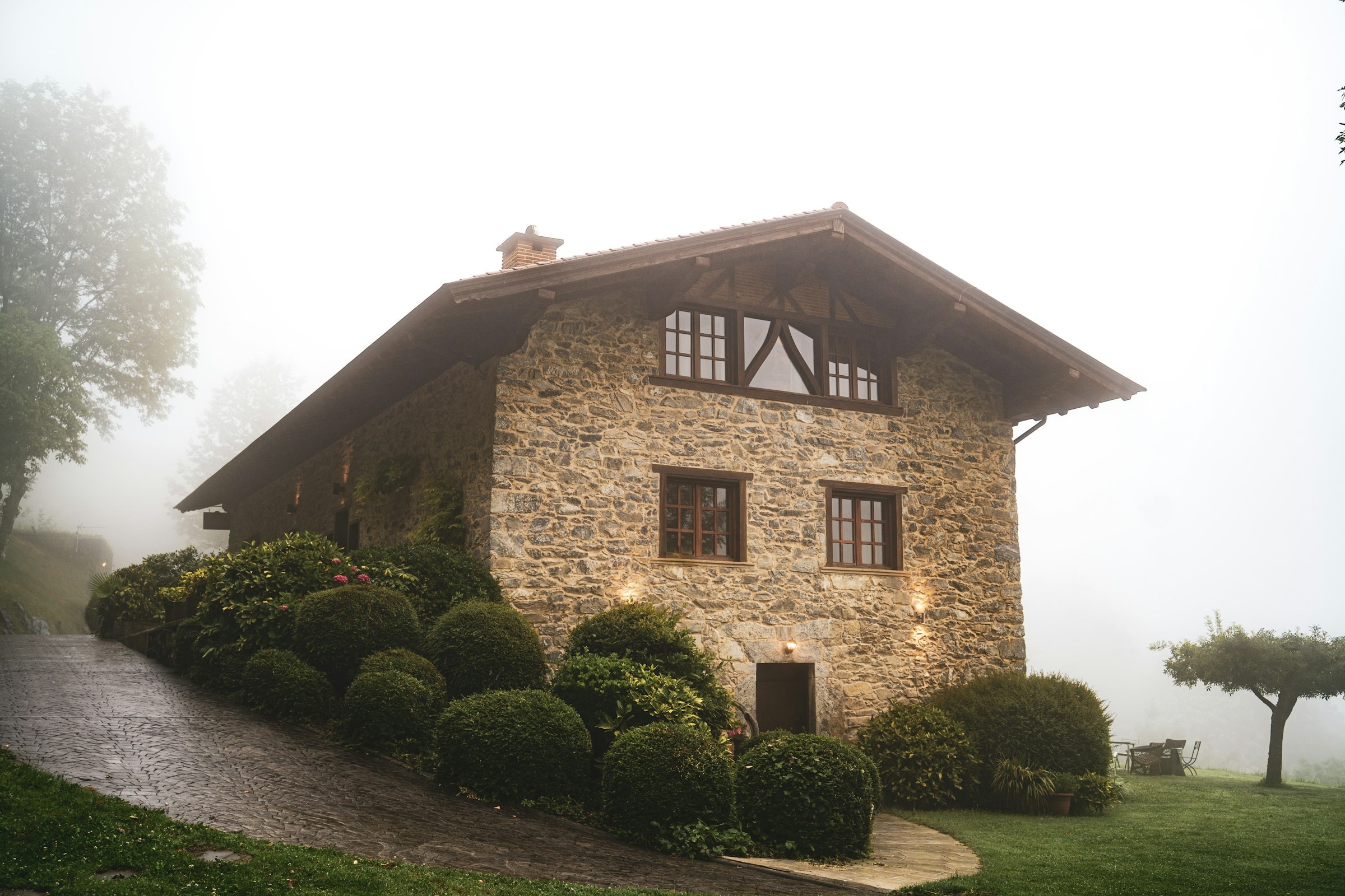 Mas Roureda, una masía de piedra de tres plantas con un gran alero de madera, asomando entre la niebla de la mañana sobre setos de boj recortados