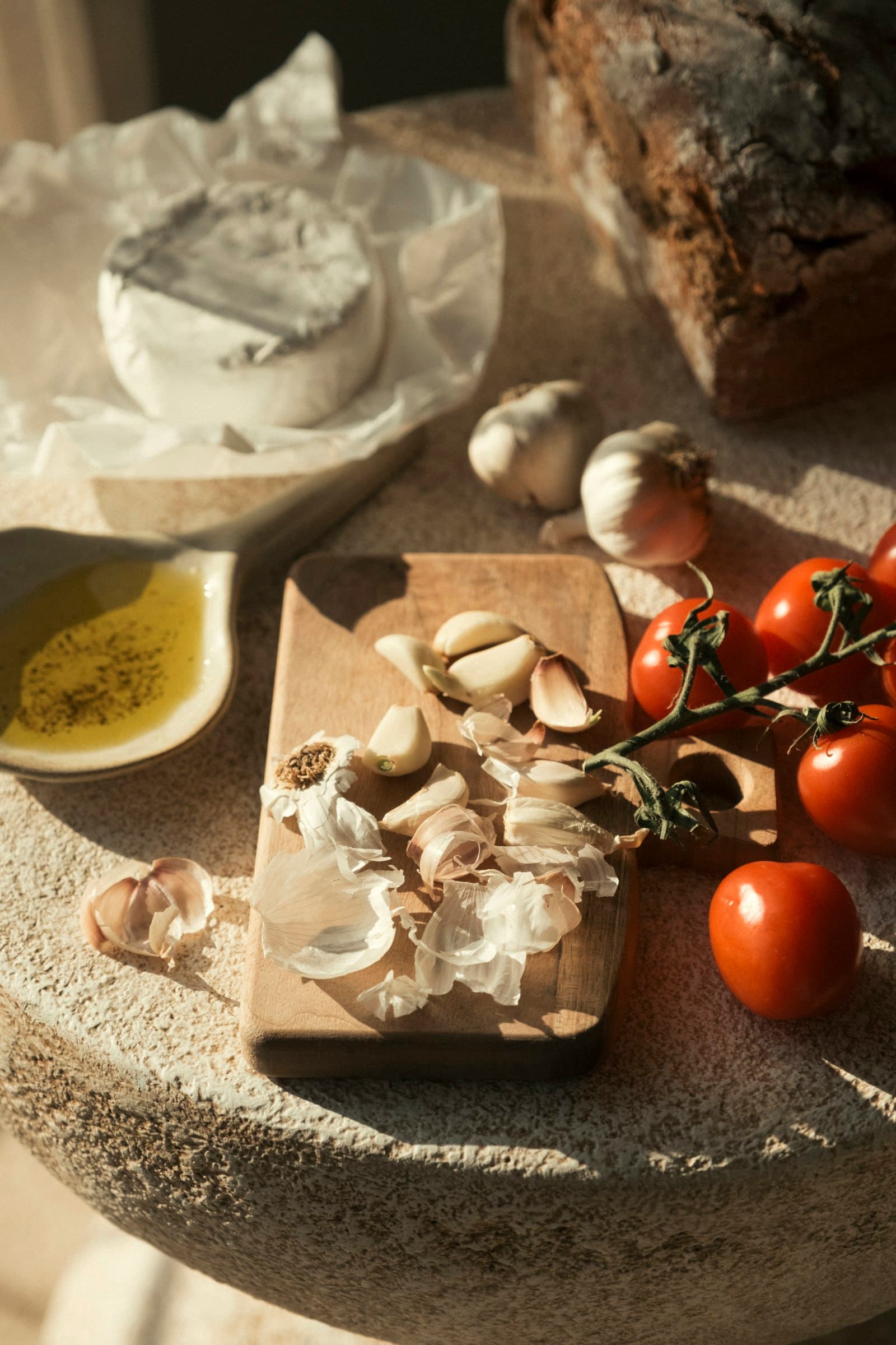 Ajos, tomates en rama, aceite de oliva, queso tierno y pan moreno sobre una mesa de piedra, con luz cálida