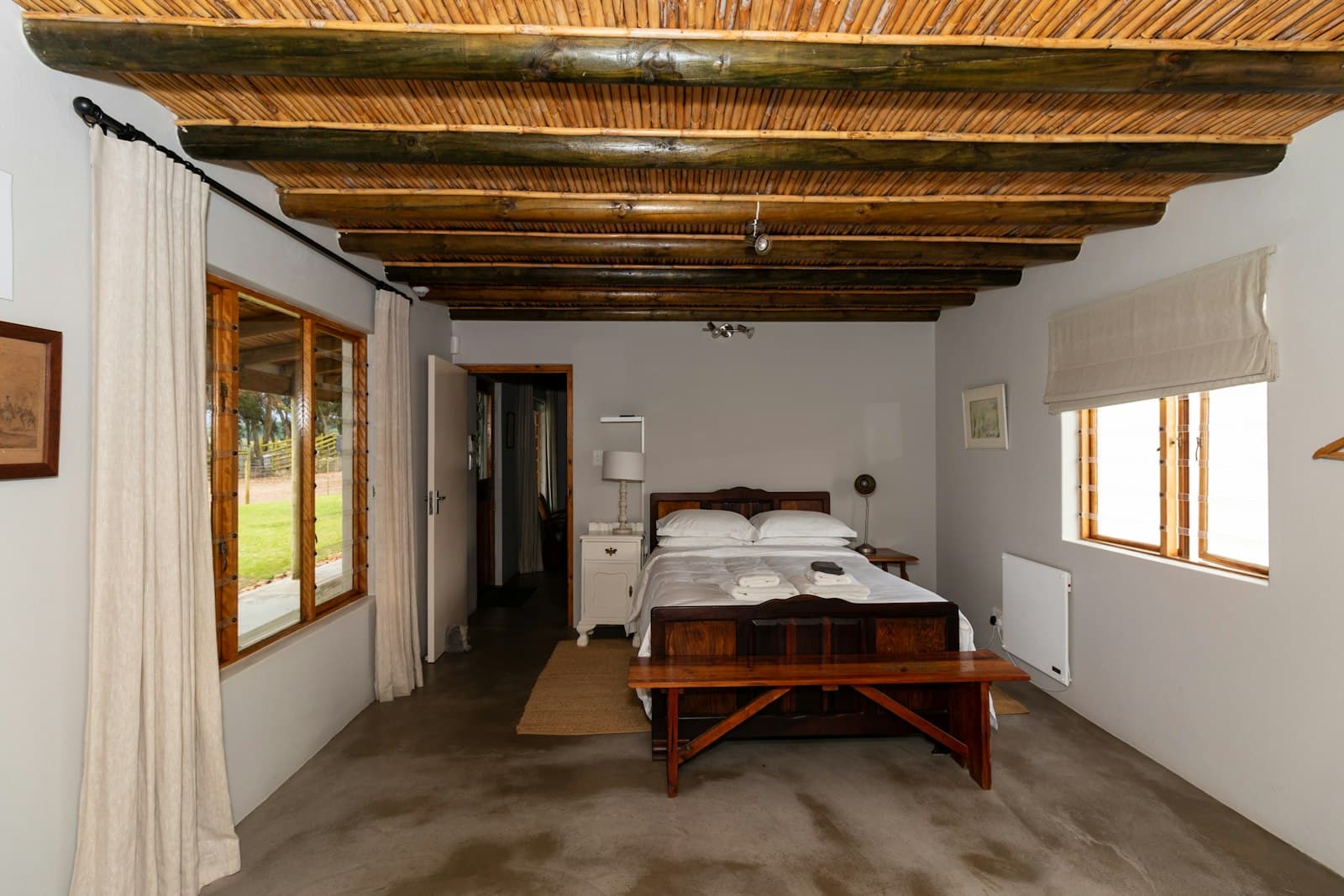 Habitación alargada en planta baja, con techo de cañizo y madera, cama antigua de madera y puertas acristaladas al jardín