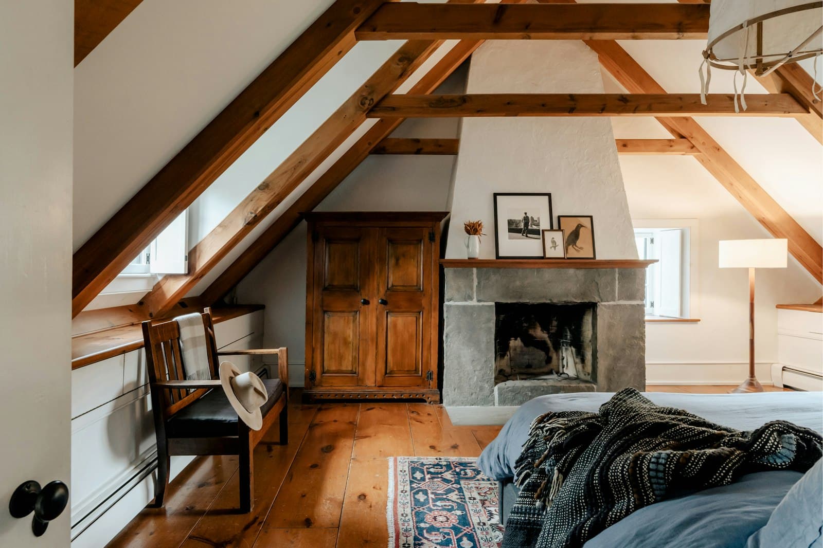 Suite en el desván bajo cerchas de madera vistas, con chimenea de piedra, armario antiguo y suelo de tablas anchas de pino